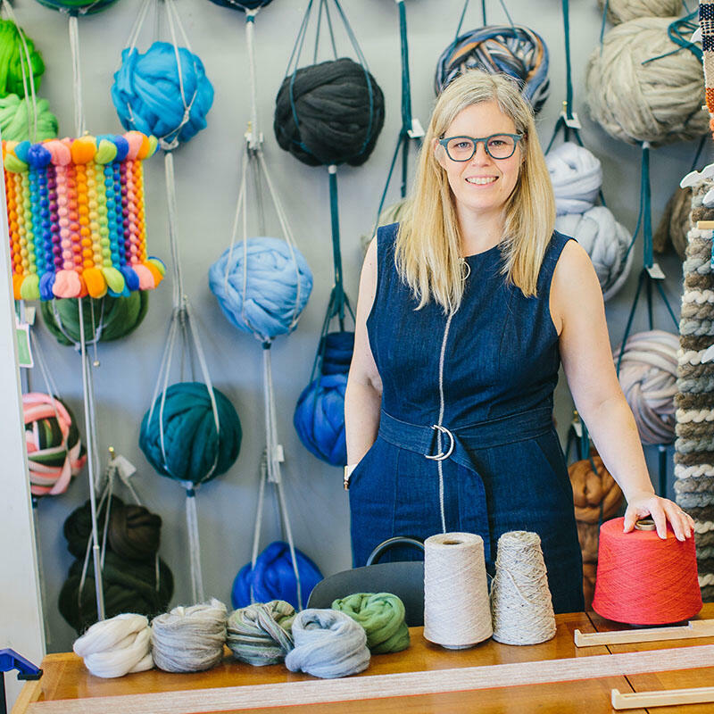 Cassandra Smith in her colourful studio of yarn and wool roving hung on the walls in planter hangers