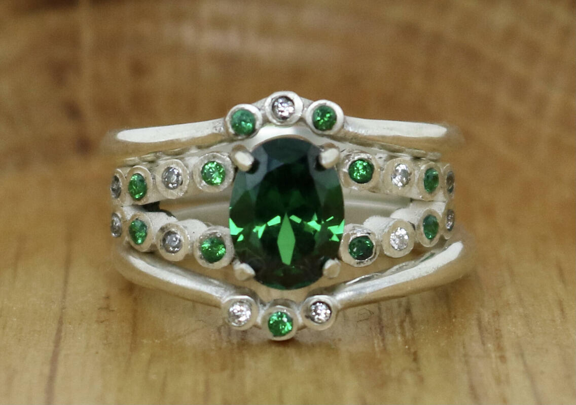 Sterling silver engagement ring with green and clear cubic zirconias paired with matching wedding bands 