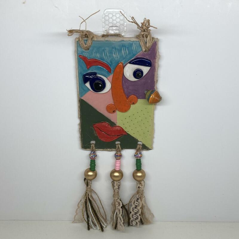 A distorted interpretation of Picasso’s Head of a Woman. From a series of ceramic and mixed media, postcard sized interpretations of well known faces. This stoneware tile is 11x16cm with raffia hair, wooden and paper beads, homemade tassels with lace and wool. The total size is 12x31cm.