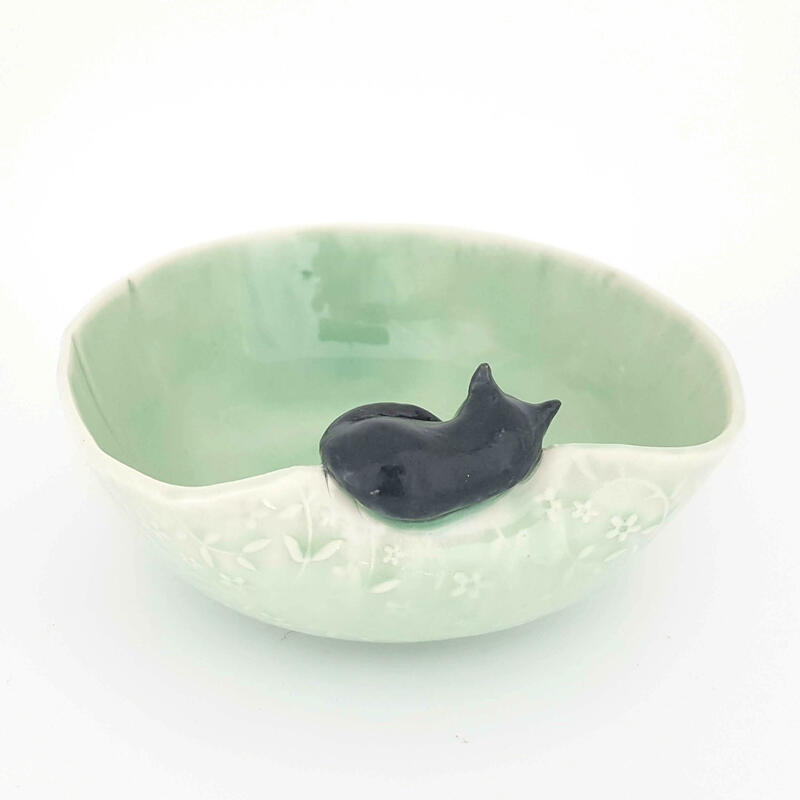 Black cat asleep on the rim of a green bowl