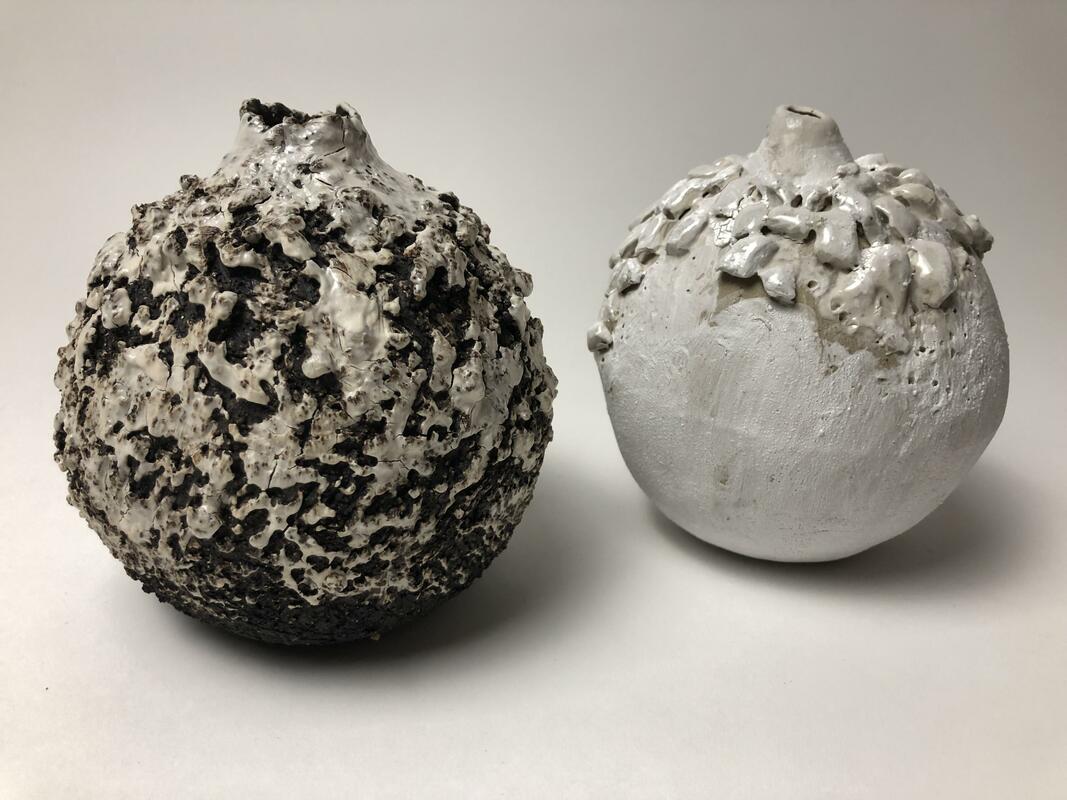 Two moon jars, one in coarse black clay with added clay texture and highlighted in white slip. The contrasting moon jar is textured with white nuggets of clay and white underglaze. Both are 15cm tall.