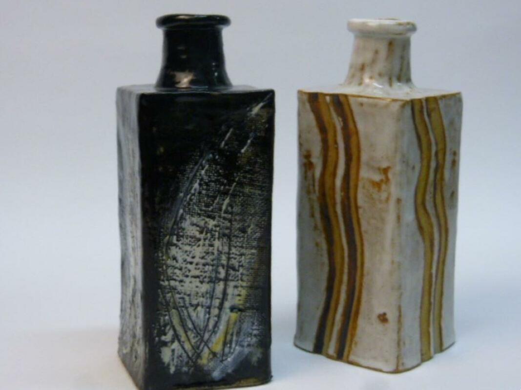 Two square section flasks, one fluted and enhanced with iron oxide, the other blaks with flourishes of white underglazes adding drama and movement.