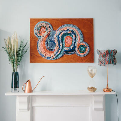 Handwoven lampshade and framed artwork in blues and orange above a mantel