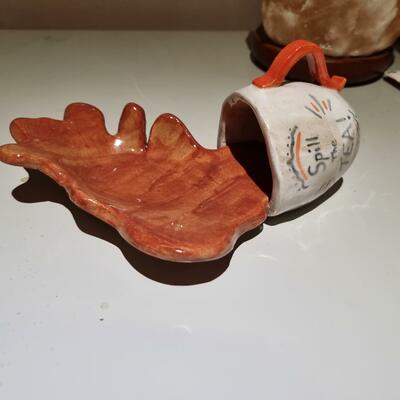 Spill the teabag holder! A ceramic teacup that has been knocked over and the ceramic tea spilling out creating a splash. this can hold your used teabags.