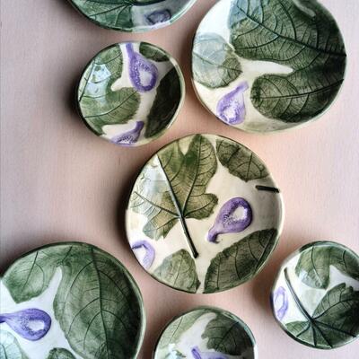 Six ceramic plates with fig and fig leaf designs displayed on a pale surface.
