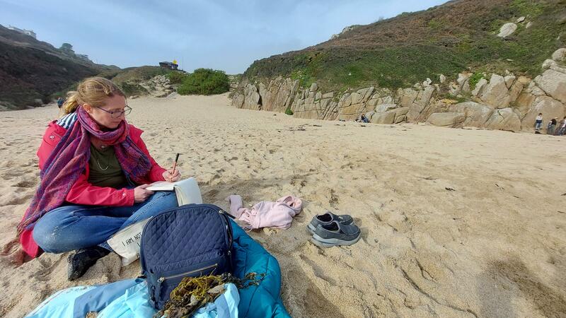 Emma Williams sat crossed legged on sandy beach in Cornwall whilst sketching