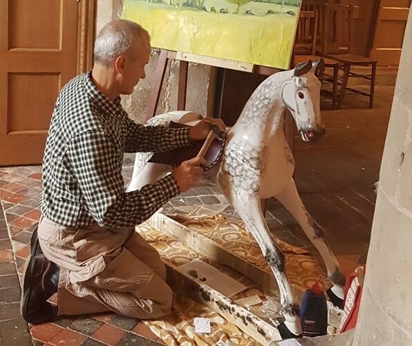 Tacking up a large, carved, gessoed and painted wooden rocking horse