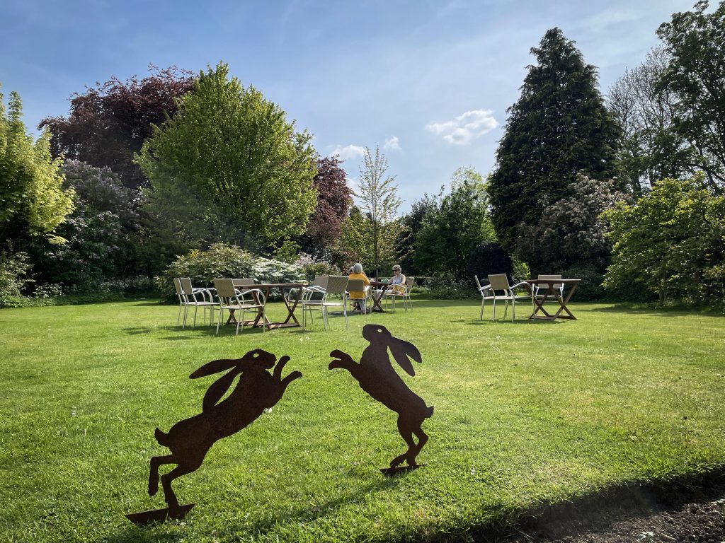 a sculpture of two hares on the green lawn of Heyford House, with tables and chairs in background