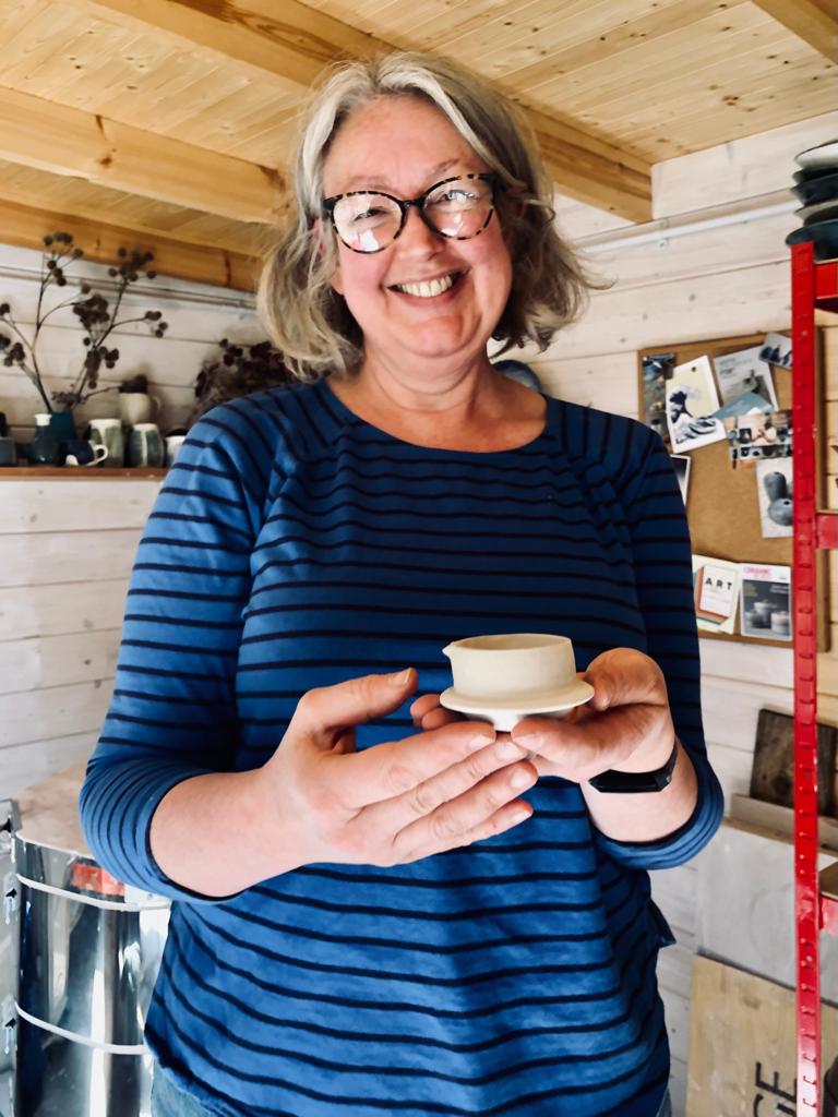 Smiling woman in shed holding teapot lid
