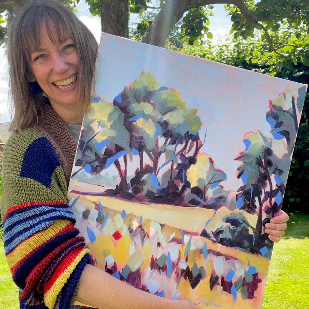 Artist Challoner Spokes, embracing a colourful landscape painting and smiling at the camera