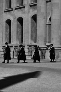 Fliss van Steenbergen: The shadow of an Oxford spire is cast across a square as graduation officials walk out.