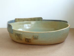 Fi Cooper: Large oval dish featuring a highly stylised lightly textured skyline, in green copper and blue cobalt washes, handbuilt