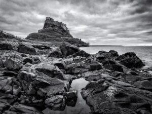Stuart Feurtado: Black and white image of Lindisfarne Abbey with foregroung rocky shoreline