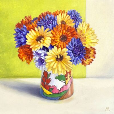 A posy of yellow, orange and gold marigolds with blue cornflowers in a Clarice Cliff vase