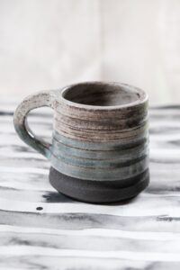 Ariadna Alvarez: Hand-thrown stoneware mug with soft blue tones and a raw clay base. A functional form defined by texture, balance, and subtle variation.